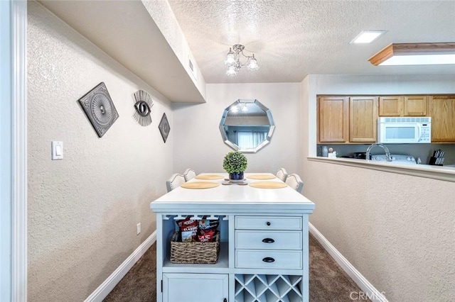 interior space featuring a textured ceiling, white microwave, dark colored carpet, and baseboards