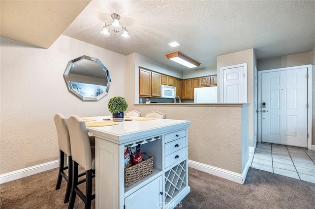 kitchen with refrigerator, white microwave, a chandelier, light carpet, and a kitchen breakfast bar