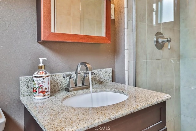 bathroom with a tile shower, a textured wall, and vanity