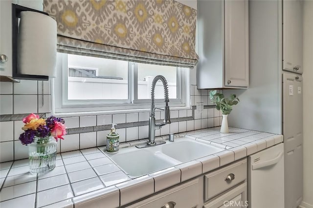 kitchen with a sink, tasteful backsplash, white dishwasher, and tile countertops