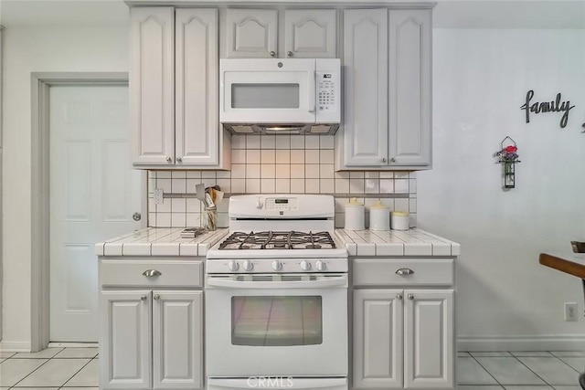kitchen with light tile patterned floors, white appliances, decorative backsplash, and tile countertops