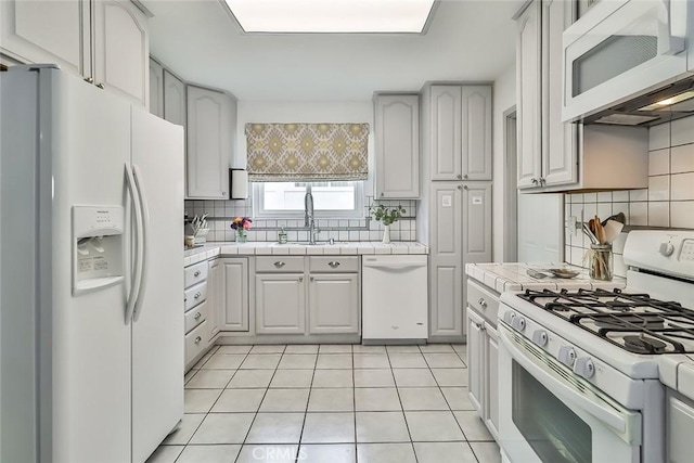 kitchen with a sink, tile counters, light tile patterned flooring, tasteful backsplash, and white appliances