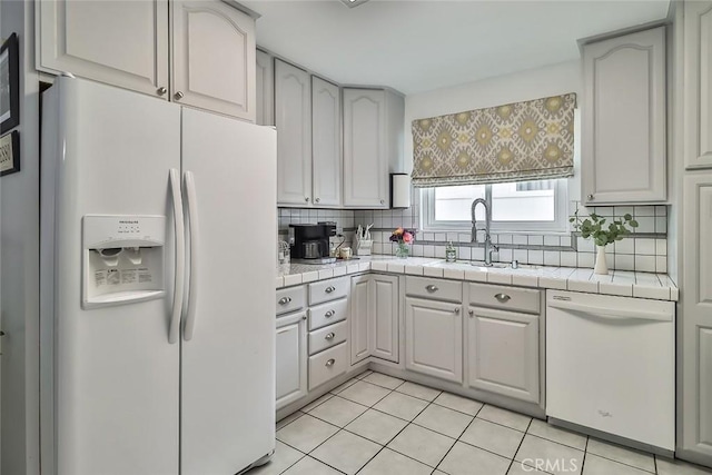 kitchen with a sink, white appliances, tasteful backsplash, and tile countertops
