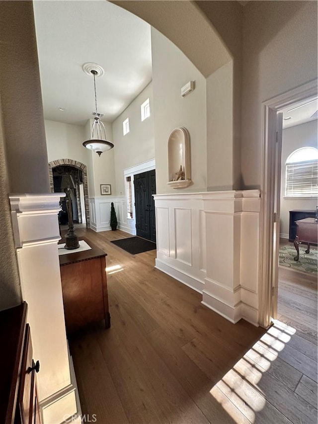 interior space with a decorative wall, hardwood / wood-style floors, wainscoting, and arched walkways