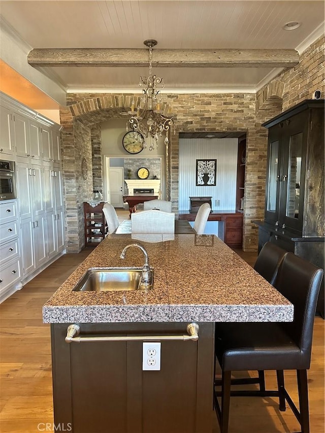 kitchen with a sink, beam ceiling, open floor plan, light wood finished floors, and a fireplace