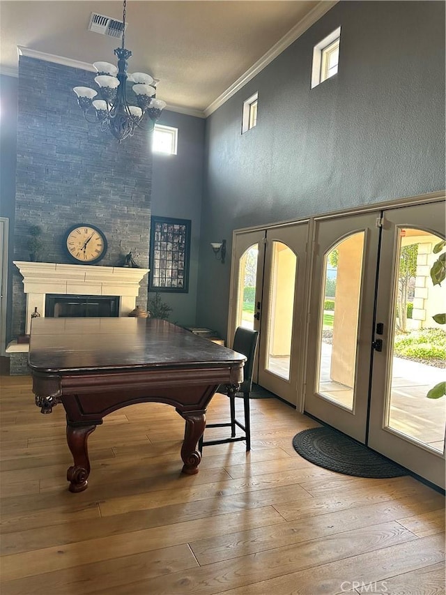rec room with hardwood / wood-style floors, ornamental molding, a glass covered fireplace, visible vents, and french doors