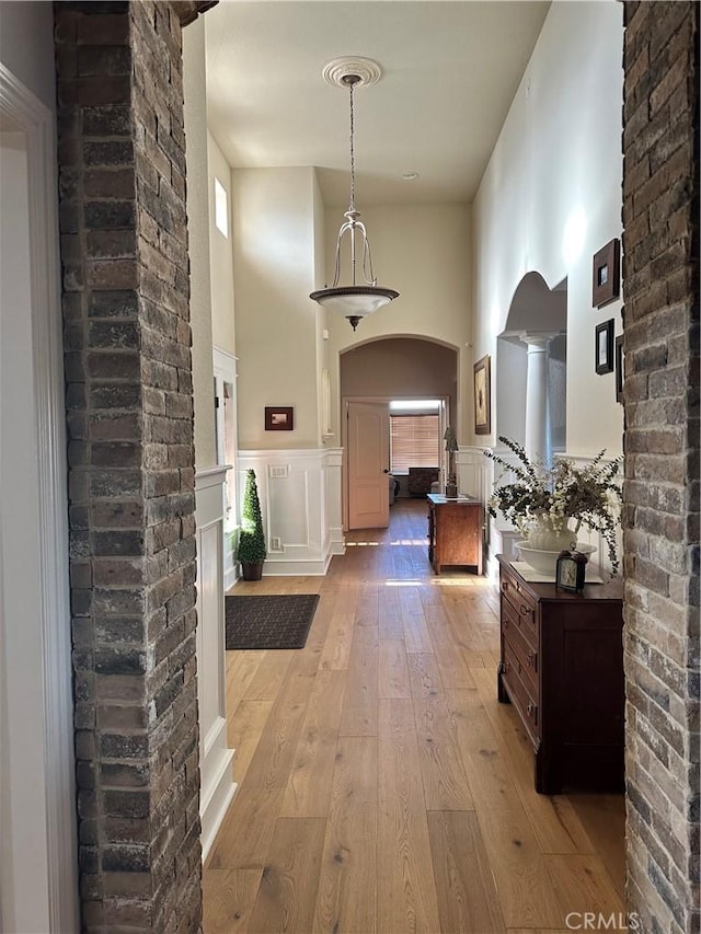 hallway with a high ceiling, a wainscoted wall, arched walkways, and light wood-style flooring
