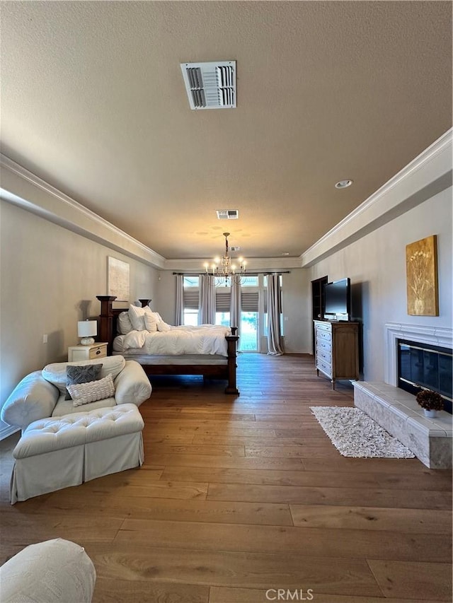 bedroom featuring a chandelier, ornamental molding, wood-type flooring, a glass covered fireplace, and visible vents