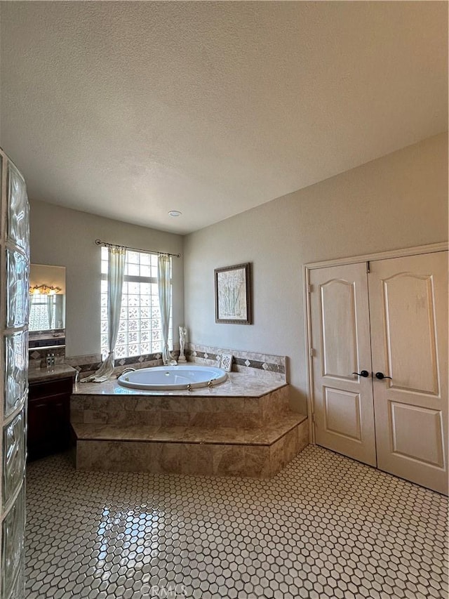 full bath with tile patterned floors, a textured ceiling, a garden tub, and vanity