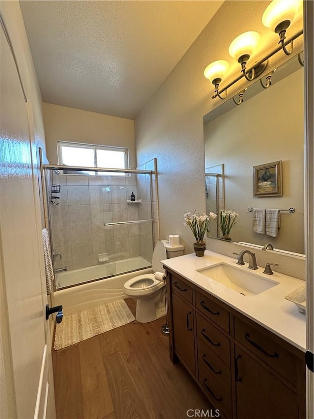 full bath with vanity, bath / shower combo with glass door, toilet, a textured ceiling, and wood finished floors