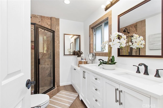 bathroom featuring a stall shower, wood finished floors, double vanity, and a sink