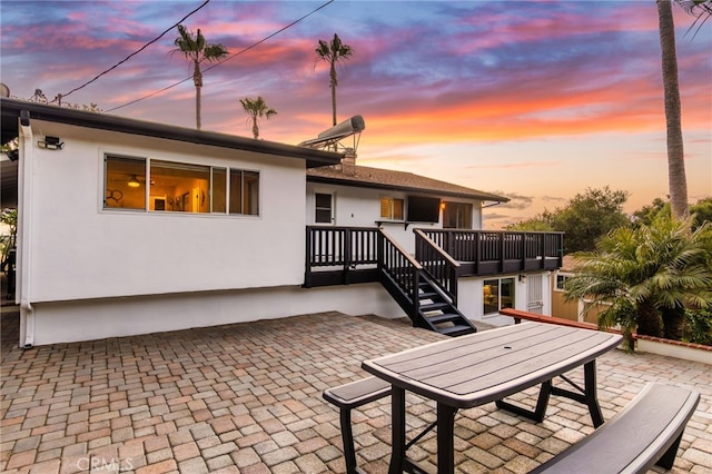 back of house at dusk featuring stairway, a wooden deck, stucco siding, and a patio area