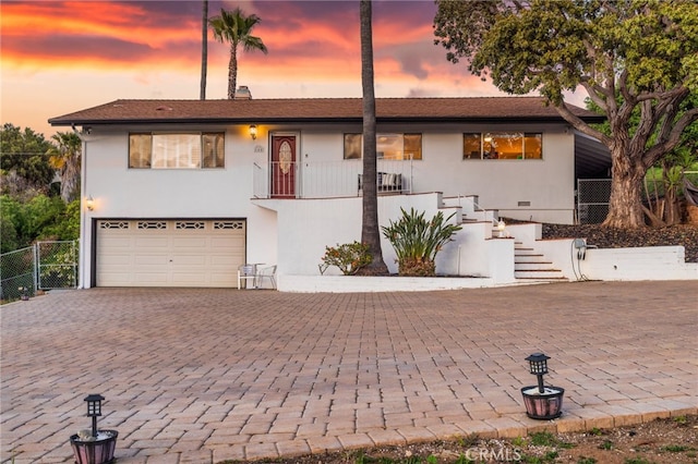 view of front of property featuring stairs, stucco siding, decorative driveway, an attached garage, and fence