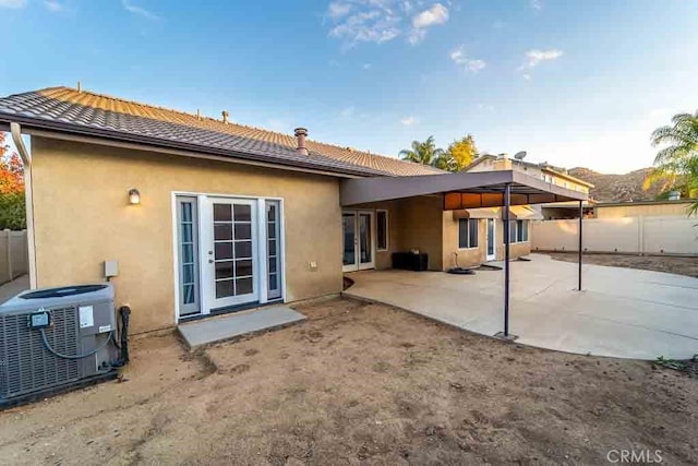 rear view of property with stucco siding, a tiled roof, fence, central air condition unit, and a patio