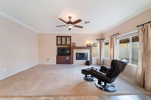 carpeted living area with visible vents, a glass covered fireplace, ceiling fan, and ornamental molding