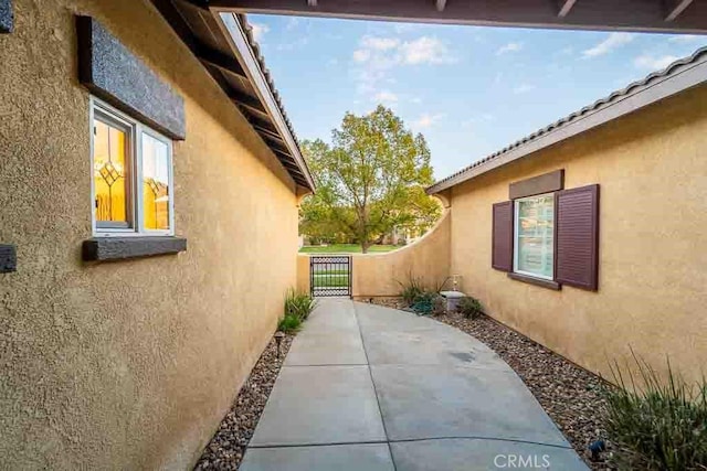 view of home's exterior with stucco siding, a gate, and a patio