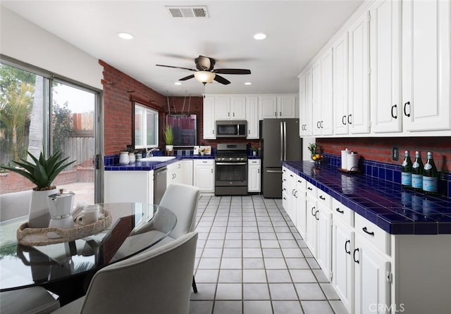 kitchen with a sink, stainless steel appliances, tile countertops, a wealth of natural light, and visible vents