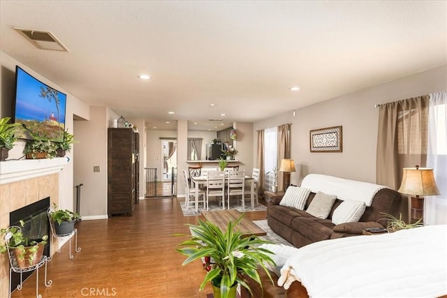 living area featuring recessed lighting, a fireplace, visible vents, baseboards, and wood finished floors