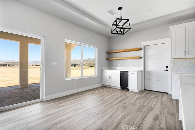 unfurnished dining area with light wood-style floors, baseboards, a notable chandelier, and visible vents