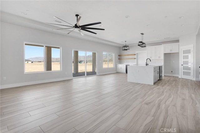 unfurnished living room featuring baseboards, ceiling fan, a sink, and light wood-style floors