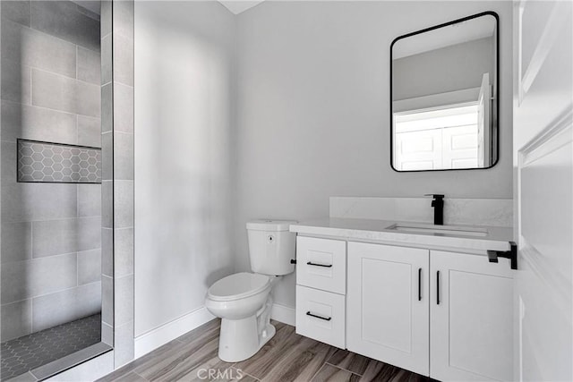 bathroom featuring vanity, wood finished floors, toilet, baseboards, and a walk in shower
