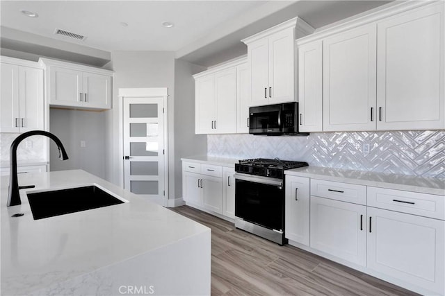 kitchen featuring gas stove, a sink, black microwave, and white cabinets