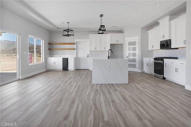 kitchen with black microwave, tasteful backsplash, gas stove, light countertops, and light wood-style flooring