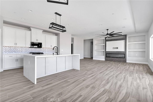 kitchen featuring baseboards, stainless steel microwave, ceiling fan, and white cabinets