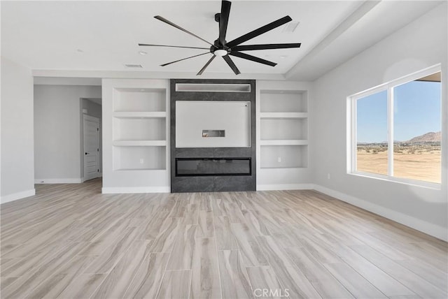 unfurnished living room with visible vents, built in features, baseboards, light wood-style floors, and ceiling fan