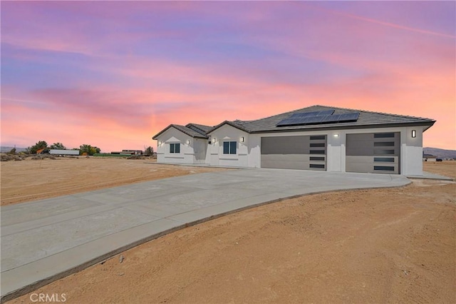 view of front of home with a garage, stucco siding, driveway, and solar panels