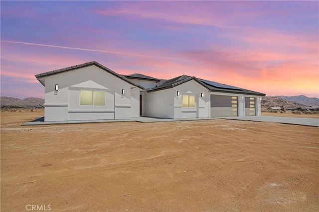ranch-style home featuring a garage, stucco siding, a mountain view, concrete driveway, and solar panels