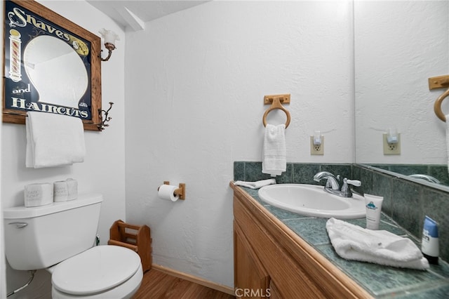half bath featuring wood finished floors, toilet, and vanity