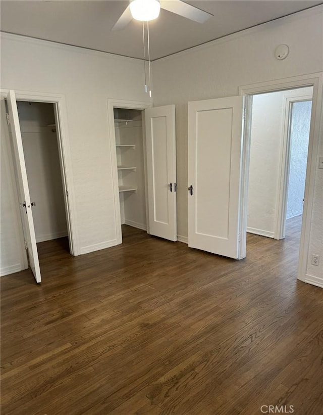unfurnished bedroom featuring ceiling fan, baseboards, multiple closets, and dark wood finished floors