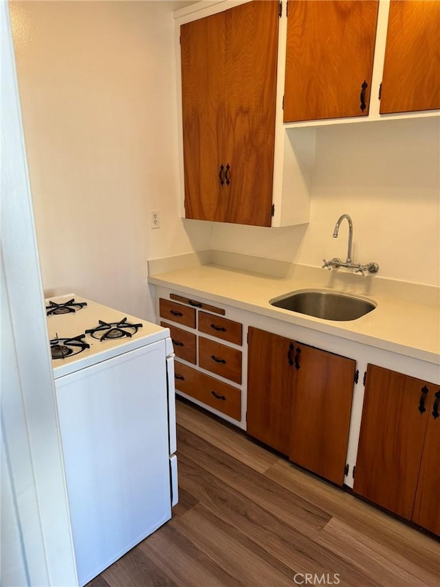 kitchen with dark wood finished floors, a sink, white gas stove, and light countertops