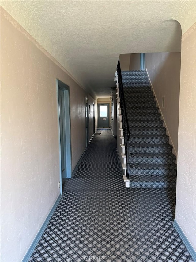 hallway with a textured ceiling, stairway, and baseboards