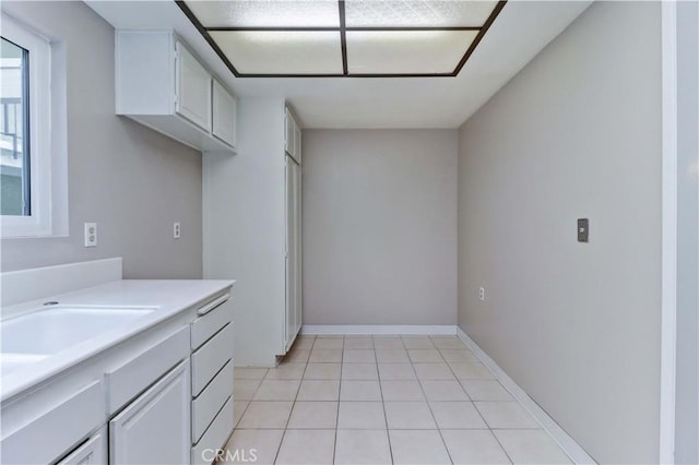 kitchen with white cabinetry, a sink, light countertops, baseboards, and light tile patterned flooring