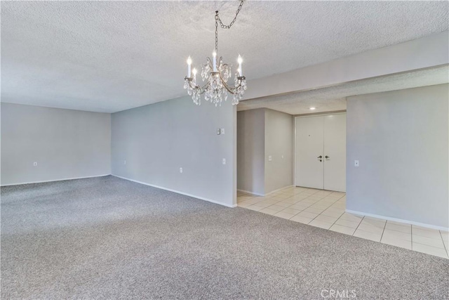 carpeted empty room featuring a textured ceiling, an inviting chandelier, tile patterned floors, and baseboards