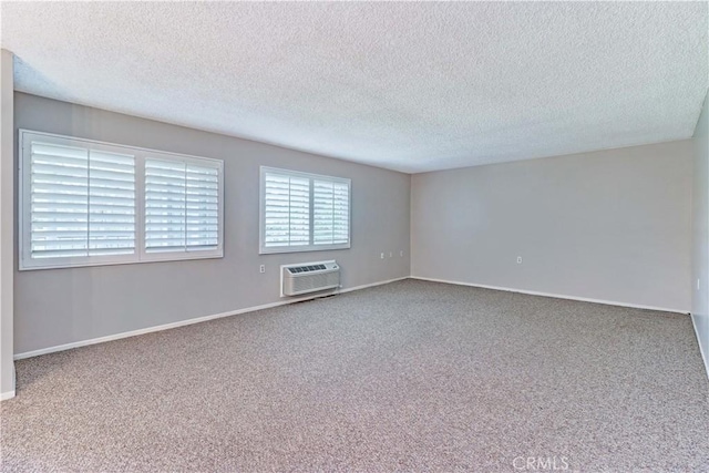 carpeted spare room with a textured ceiling, a wall mounted AC, and baseboards