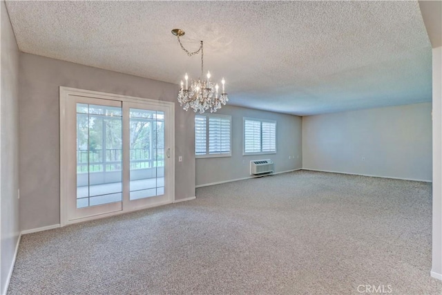 carpeted empty room featuring an AC wall unit, an inviting chandelier, a textured ceiling, and baseboards