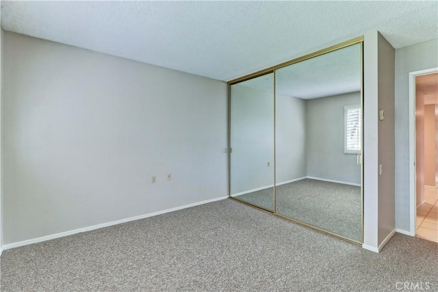 unfurnished bedroom featuring a textured ceiling, baseboards, carpet flooring, and a closet