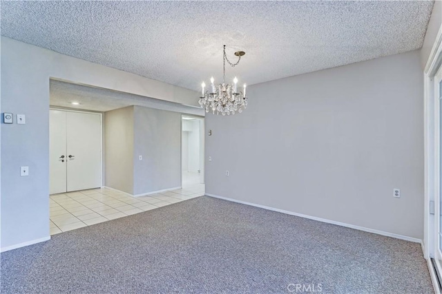 carpeted empty room with tile patterned floors, a textured ceiling, a chandelier, and baseboards