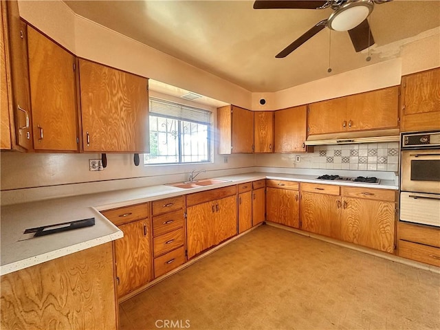 kitchen with a sink, brown cabinets, a warming drawer, light countertops, and wall oven