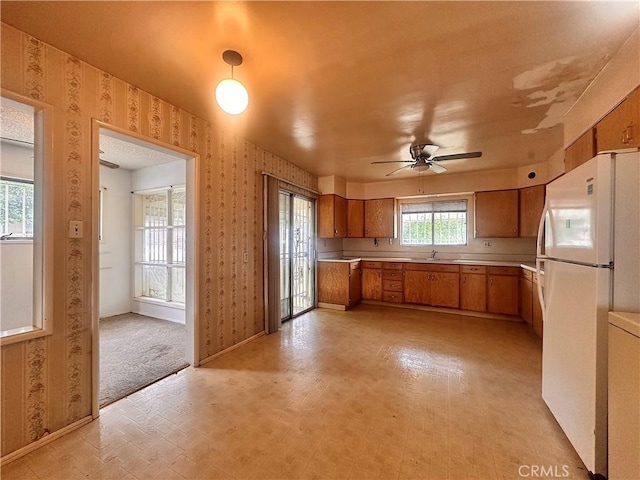 kitchen with wallpapered walls, brown cabinets, light countertops, and freestanding refrigerator