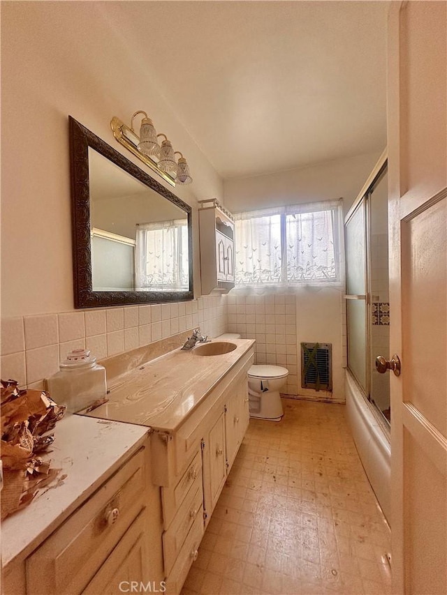 full bathroom with combined bath / shower with glass door, toilet, tile walls, tile patterned floors, and vanity