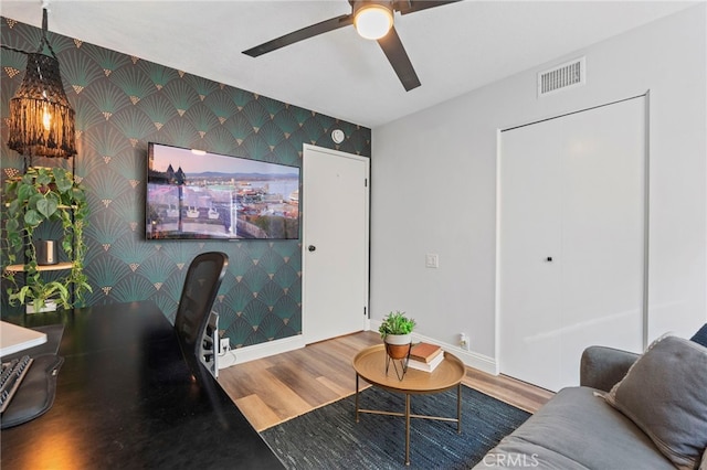 office featuring visible vents, baseboards, an accent wall, wallpapered walls, and wood finished floors