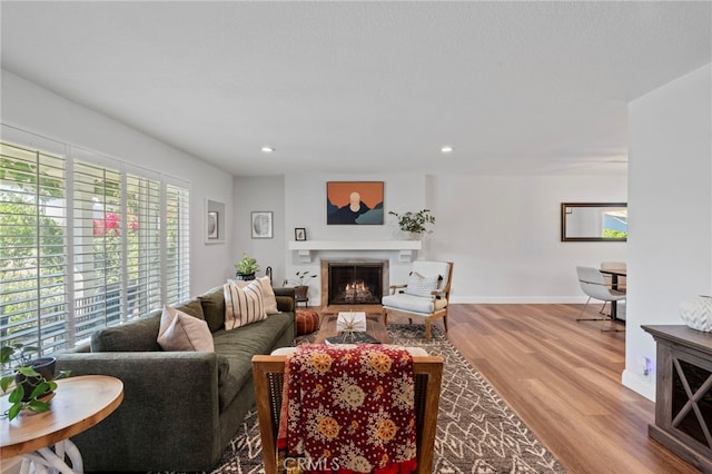 living area featuring baseboards, recessed lighting, wood finished floors, and a lit fireplace