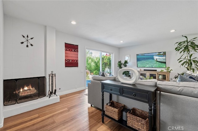 living area featuring a tiled fireplace, recessed lighting, light wood-style flooring, and baseboards