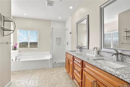 bathroom with a stall shower, double vanity, a bath, and a sink