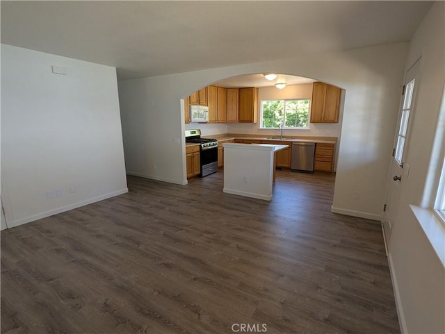 kitchen featuring appliances with stainless steel finishes, light countertops, arched walkways, dark wood-style flooring, and open floor plan