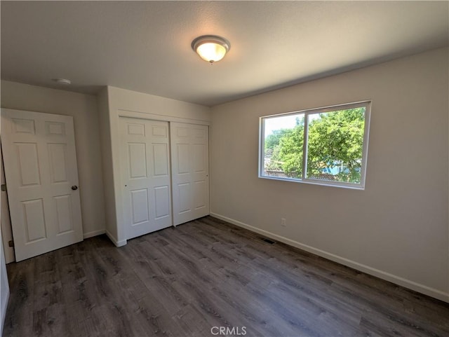 unfurnished bedroom featuring dark wood-type flooring, a closet, visible vents, and baseboards